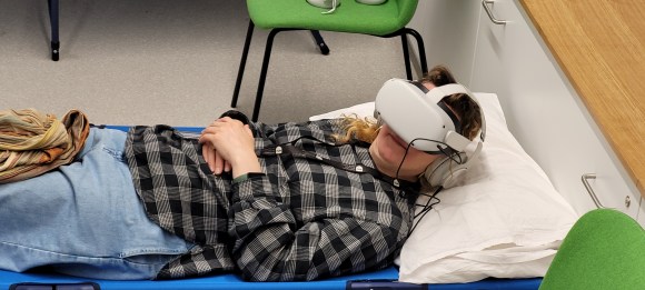 Woman laying with head on pillow. Wearing VR headset and headphones. Looking relaxed